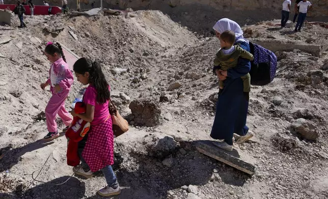 A family cross into Syria on foot, through a crater caused by Israeli airstrikes aiming to block Beirut-Damascus highway at the Masnaa crossing, in the eastern Bekaa Valley, Lebanon, Saturday, Oct. 5, 2024. (AP Photo/Hassan Ammar)