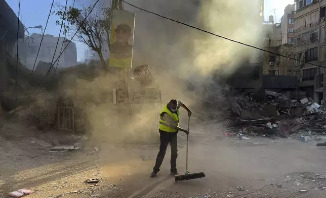 A worker cleans a street as smoke rises from a destroyed building that was hit by an Israeli airstrike in Dahiyeh, in the southern suburb of Beirut, Lebanon, early Sunday, Oct. 20, 2024. (AP Photo/Hussein Malla)