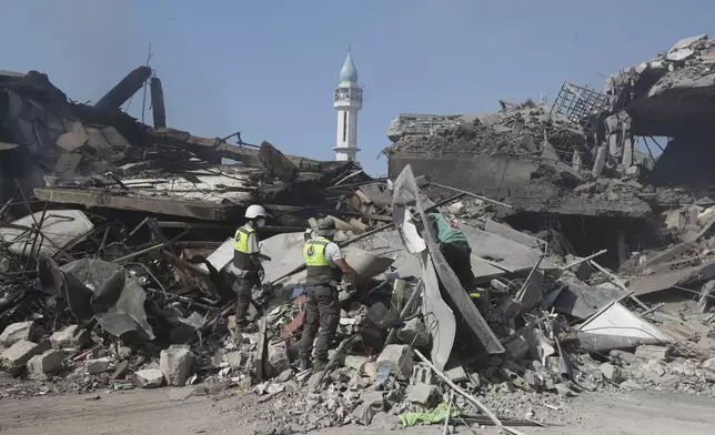 Hezbollah rescue workers search for victims on the rubble of destroyed buildings at commercial street that was hit Saturday night by Israeli airstrikes, in NAbatiyeh town, south Lebanon, Sunday, Oct. 13, 2024. (AP Photo/Mohammed Zaatari)