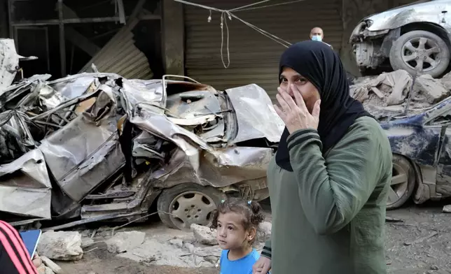 A woman passes in front of destroyed cars at the site of Thursday's Israeli airstrike, in Beirut, Lebanon, Friday, Oct. 11, 2024. (AP Photo/Hussein Malla)