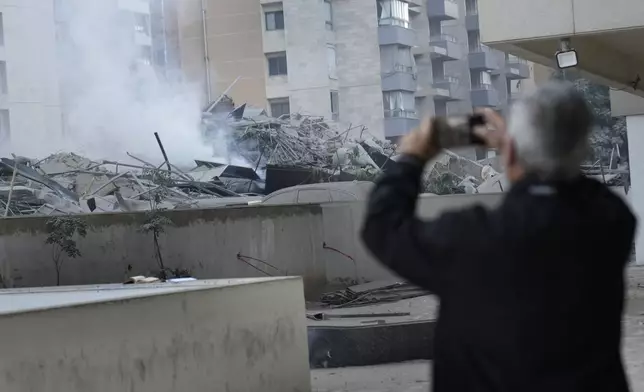 A man takes pictures with his mobile phone of a destroyed resident complex where he lives that hit by an Israeli airstrike in Dahieh, Beirut, Lebanon, Wednesday, Oct. 2, 2024. (AP Photo/Hussein Malla)