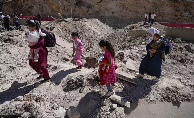 People carry their luggage as they cross into Syria on foot, through a crater caused by Israeli airstrikes aiming to block Beirut-Damascus highway at the Masnaa crossing, in the eastern Bekaa Valley, Lebanon, Saturday, Oct. 5, 2024. (AP Photo/Hassan Ammar)