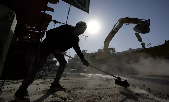 A man clears debris from a street in front of a destroyed building that was hit Tuesday night in an Israeli airstrike, in the southern port city of Sidon, Lebanon, Wednesday, Oct. 30, 2024. (AP Photo/Bilal Hussein)