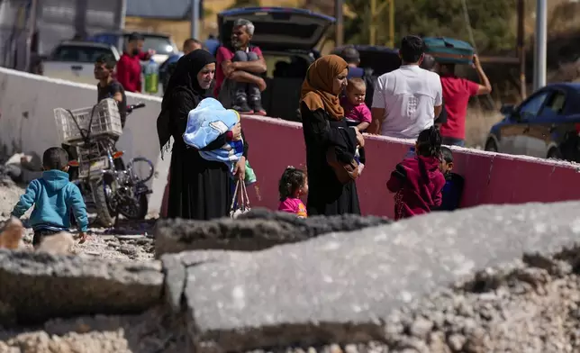 People carry their luggage as they cross into Syria on foot, through a crater caused by Israeli airstrikes aiming to block Beirut-Damascus highway at the Masnaa crossing, in the eastern Bekaa Valley, Lebanon, Saturday, Oct. 5, 2024. (AP Photo/Hassan Ammar)