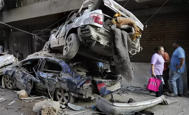 A Lebanese woman passes next of destroyed cars at the site of Thursday's Israeli airstrike, in Beirut, Lebanon, Friday, Oct. 11, 2024. (AP Photo/Hussein Malla)