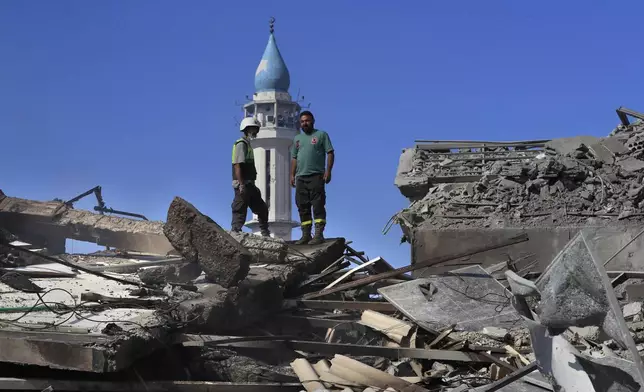 A Hezbollah rescue worker, left, and a Lebanese Civil Defence worker, right, stand on the rubble of destroyed buildings at commercial street that was hit Saturday night by Israeli airstrikes, in NAbatiyeh town, south Lebanon, Sunday, Oct. 13, 2024. (AP Photo/Mohammed Zaatari)