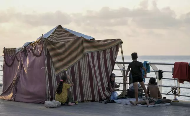 A displaced family fleeing the Israeli airstrikes in the south, sits next to their tent on Beirut's corniche, Lebanon, Monday, Oct. 14, 2024. (AP Photo/Bilal Hussein)