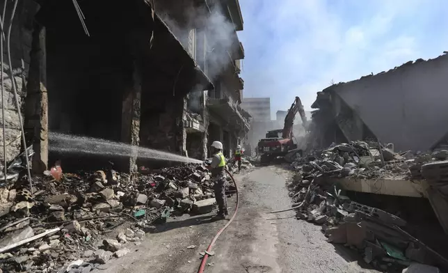 A Hezbollah firefighter hoses down on burned and destroyed shops at a commercial street that was hit Saturday night by Israeli airstrikes, in Nabatiyeh town, south Lebanon, Sunday, Oct. 13, 2024. (AP Photo/Mohammed Zaatari)