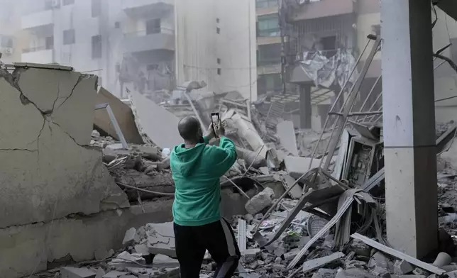 A man takes pictures by his mobile phone of a destroyed building hit by an Israeli airstrike in Dahieh, Beirut, Lebanon, Wednesday, Oct. 2, 2024. (AP Photo/Hussein Malla)