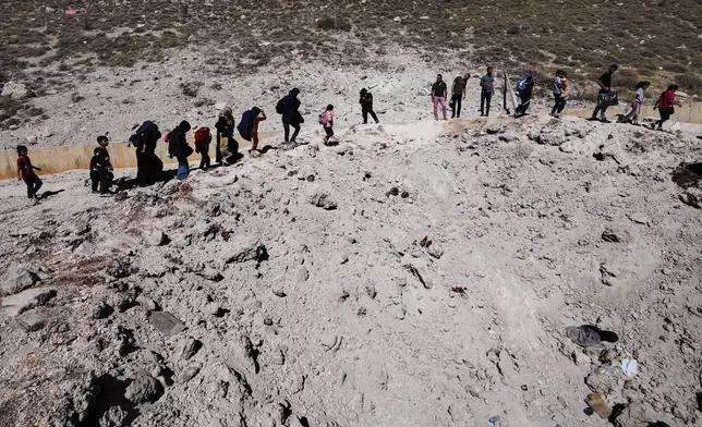 People carry their luggage as they cross into Syria on foot, through a crater caused by Israeli airstrikes aiming to block Beirut-Damascus highway at the Masnaa crossing, in the eastern Bekaa Valley, Lebanon, Saturday, Oct. 5, 2024. (AP Photo/Hassan Ammar)