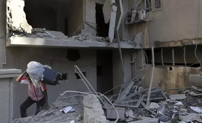 A man carries a luggage as he walks on the rubble of destroyed apartments that were hit by Israeli airstrikes, in Tyre, south Lebanon, Thursday, Oct. 24, 2024. (AP Photo/Mohammed Zaatari)