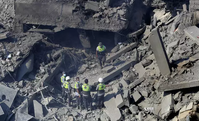 Hezbollah rescue workers stand on the rubble of destroyed buildings at commercial street that was hit Saturday night by Israeli airstrikes, in NAbatiyeh town, south Lebanon, Sunday, Oct. 13, 2024. (AP Photo/Mohammed Zaatari)