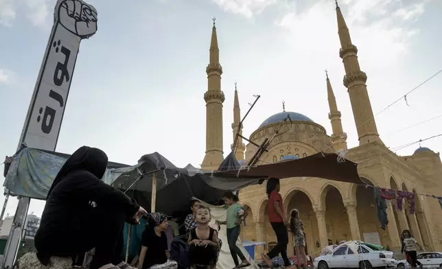 Families fleeing the Israeli airstrikes in the south, sit in front of the Mohammad al-Amin Mosque in downtown Beirut, Lebanon, Monday, Oct. 14, 2024. (AP Photo/Bilal Hussein)