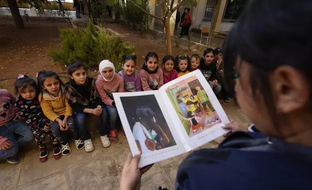 Displaced children, who fled Baalbek city and the nearby towns of Douris and Ain Bourday with their families amid the ongoing Hezbollah-Israel war, listen to a story at a school being used as a shelter, in Deir Al-Ahmar, east Lebanon, Thursday, Oct. 31, 2024. (AP Photo/Hassan Ammar)