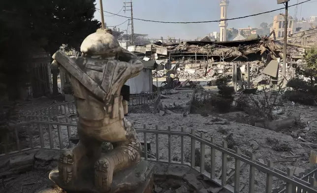 Destroyed shops are seen in front of a Hezbollah fighter statue on a commercial street that was hit Saturday night by Israeli airstrikes, in NAbatiyeh town, south Lebanon, Sunday, Oct. 13, 2024. (AP Photo/Mohammed Zaatari)