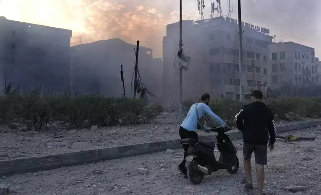 A man pushes his scooter in front of destroyed buildings hit by Israeli airstrikes in Dahiyeh, Beirut, Lebanon, Sunday, Oct. 6, 2024. (AP Photo/Hussein Malla)