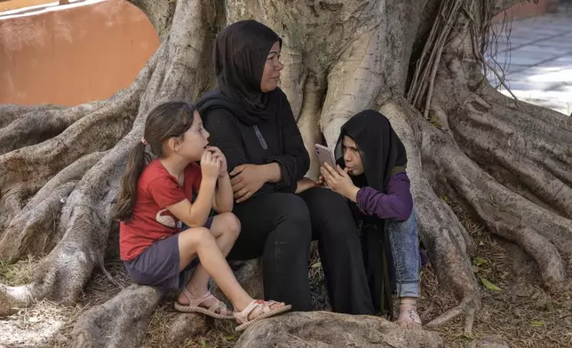 A displaced woman sits with her daughters at a vocational training center run by the U.N. agency for Palestinian refugees, or UNRWA, in the southern town of Sebline, south of Beirut, Lebanon, Friday, Oct. 4, 2024, after fleeing the Israeli airstrikes in the south. (AP Photo/Bilal Hussein)