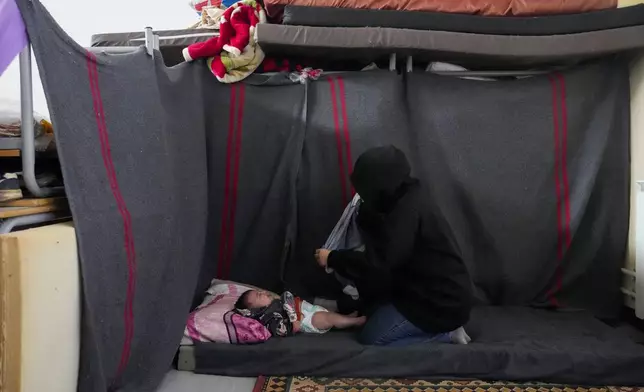 A displaced woman, who fled Baalbek city and the nearby towns of Douris and Ain Bourday amid the ongoing Hezbollah-Israel war, changes the diaper of her daughter at a school being used as a shelter, in Deir Al-Ahmar, east Lebanon, Thursday, Oct. 31, 2024. (AP Photo/Hassan Ammar)