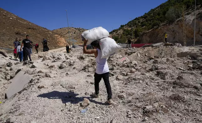 People carry their luggage as they cross into Syria on foot, through a crater caused by Israeli airstrikes aiming to block Beirut-Damascus highway at the Masnaa crossing, in the eastern Bekaa Valley, Lebanon, Saturday, Oct. 5, 2024. (AP Photo/Hassan Ammar)