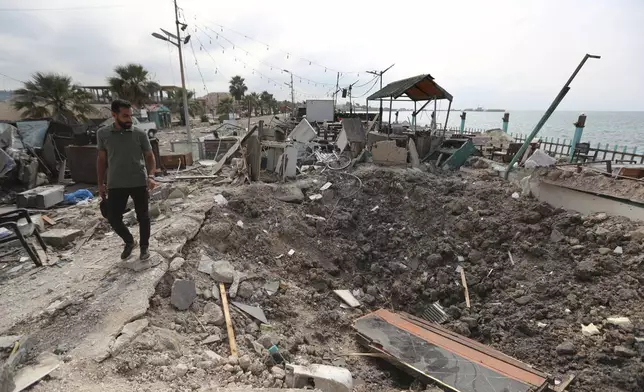 A man walks past a crater caused by an Israeli airstrike that hit a seaside coffee shop in Ghaziyeh town, south Lebanon, Sunday Oct. 6, 2024. (AP Photo/Mohammed Zaatari)