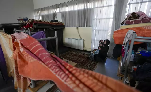 A displaced woman, who fled Baalbek city and the nearby towns of Douris and Ain Bourday amid the ongoing Hezbollah-Israel war, holds her daughter at a school being used as a shelter, in Deir Al-Ahmar, east Lebanon, Thursday, Oct. 31, 2024. (AP Photo/Hassan Ammar)