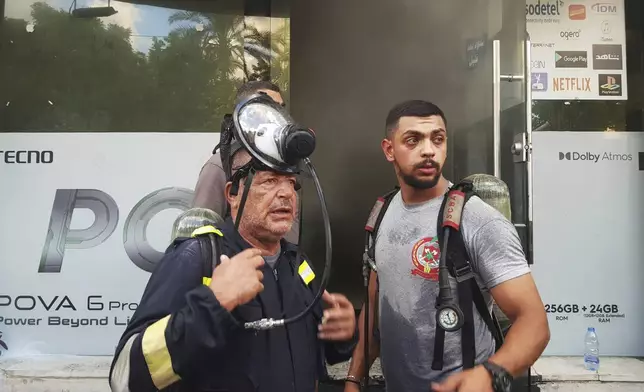 FILE - Firefighters stand outside a damaged mobile shop after what is believed to be the result of a walkie-talkies exploding inside it, in the southern port city of Sidon, Lebanon, Wednesday, Sept. 18, 2024. (AP Photo/Mohammed Zaatari, File)