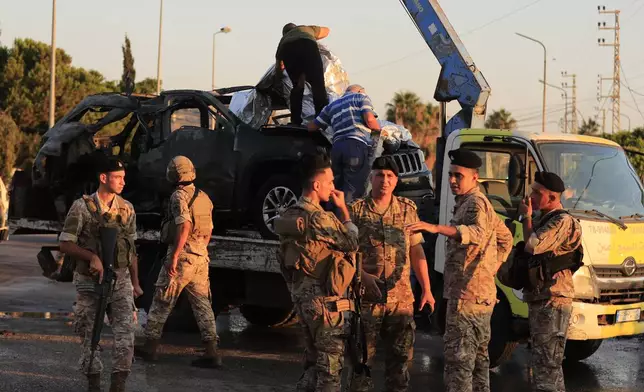 FILE - Lebanese army soldiers stand guard in front of a car that was hit by an Israeli strike as workers covered it on a truck, in the southern port city of Sidon, Lebanon, Friday, Aug. 9, 2024. (AP Photo/Mohammed Zaatari, File)