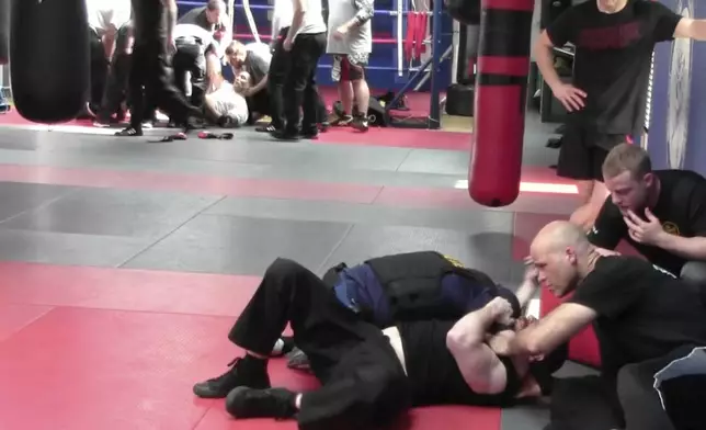 In this image from video made by the Evansville Police Department, rookie sheriff’s Deputy Asson Hacker, background left, lies unconscious after training with Mike Fisher, a sheriff's major from a nearby county, as another recruit undergoes training, foreground, during "Big Fight " day for the Southwest Indiana Law Enforcement Academy in Evansville, Ind., on March 2, 2023. (Evansville Police Department via AP)