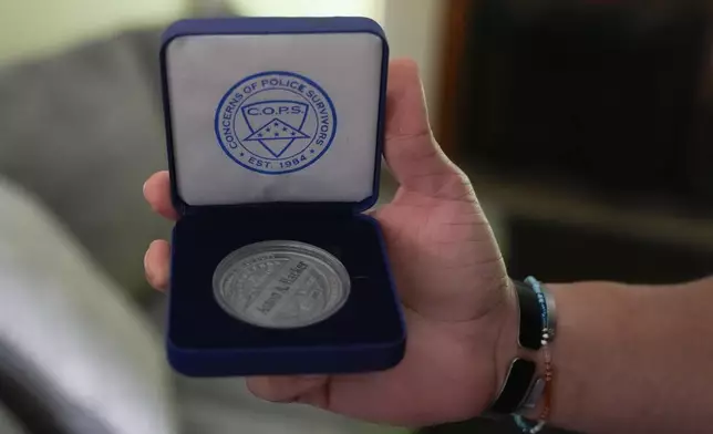 Lij Hacker holds a coin inscribed with the name of his late brother, Asson Hacker, during an interview in Bloomington, Ind., on June 4, 2024. (AP Photo/Darron Cummings)