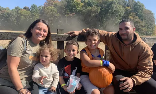 In this photo provided by the family, Asson Hacker, right, sits with his wife and their children during a trip to the Mayse Farm pumpkin patch in Evansville, Ind., in October 2022. (Family photo via AP)