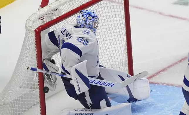 Tampa Bay Lightning goaltender Andrei Vasilevskiy reaches behind his back to block a shot in the third period of an NHL hockey game against the Colorado Avalanche, Wednesday, Oct. 30, 2024, in Denver. (AP Photo/David Zalubowski)