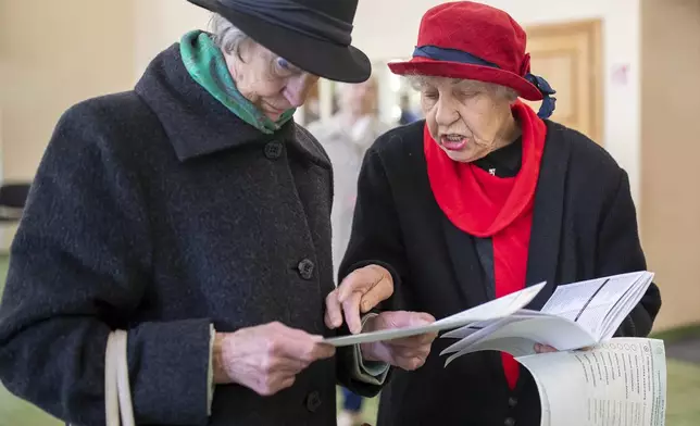 Women read ballot papers at a polling station during a first round of voting in parliamentary election, in Vilnius, Lithuania, Sunday, Oct. 13, 2024. (AP Photo/Mindaugas Kulbis)