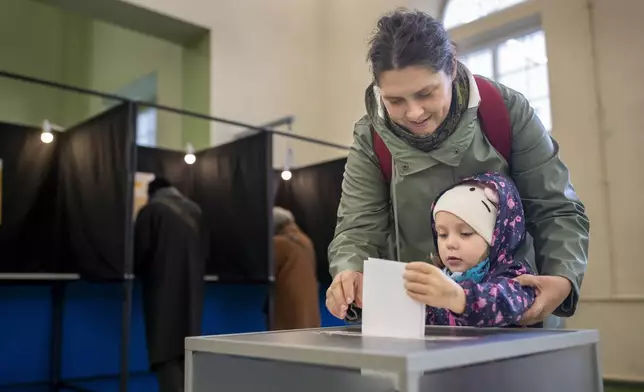 A woman with a child casts a ballot at a polling station during the first round of voting in parliamentary elections, in Vilnius, Lithuania, Sunday, Oct. 13, 2024. (AP Photo/Mindaugas Kulbis)