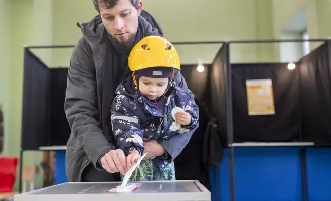 A man with a child casts his ballot at a polling station during the first round of voting in parliamentary elections, in Vilnius, Lithuania, Sunday, Oct. 13, 2024. (AP Photo/Mindaugas Kulbis)