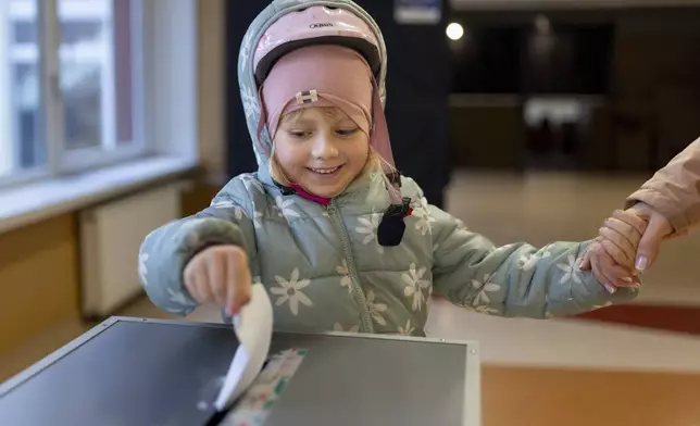 A girl helps to cast a ballot at a polling station during a second round of voting in parliamentary election, in Vilnius, Lithuania, Sunday, Oct. 27, 2024. (AP Photo/Mindaugas Kulbis)