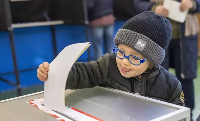 A boy casts a ballot at a polling station during the first round of voting in parliamentary election, in Vilnius, Lithuania, Sunday, Oct. 13, 2024. (AP Photo/Mindaugas Kulbis)