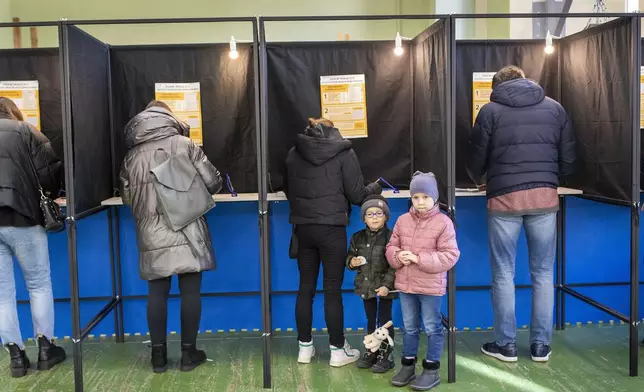 A children stand near a voting booth during the first round of voting in parliamentary election, in Vilnius, Lithuania, Sunday, Oct. 13, 2024. (AP Photo/Mindaugas Kulbis)