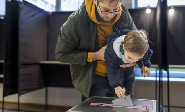 A man with a child casts a ballot at a polling station during a second round of voting in parliamentary election, in Vilnius, Lithuania, Sunday, Oct. 27, 2024. (AP Photo/Mindaugas Kulbis)