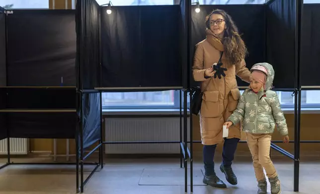 A woman with a child prepare to cast a ballot at a polling station during a second round of voting in parliamentary election, in Vilnius, Lithuania, Sunday, Oct. 27, 2024. (AP Photo/Mindaugas Kulbis)