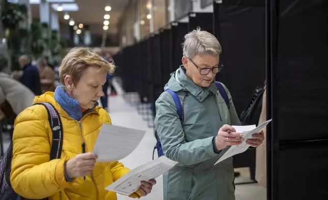 Women read a ballot paper at a polling station during the advance voting in the first round of a parliamentary election in Vilnius, Lithuania, Wednesday, Oct. 9, 2024. (AP Photo/Mindaugas Kulbis)