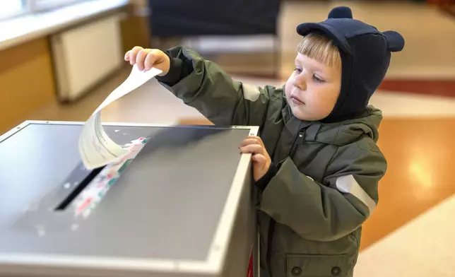 A boy helps to cast a ballot at a polling station during a second round of voting in parliamentary election, in Vilnius, Lithuania, Sunday, Oct. 27, 2024. (AP Photo/Mindaugas Kulbis)