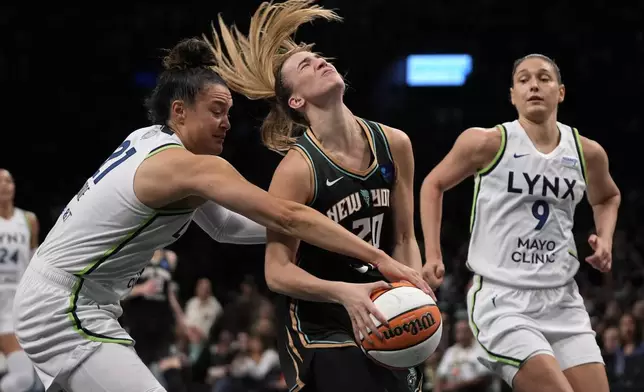 New York Liberty's Sabrina Ionescu, center, falls while dribbling against Minnesota Lynx's Kayla McBride, left, during the first half in Game 2 of a WNBA basketball final playoff series, Sunday, Oct. 13, 2024, in New York. (AP Photo/Pamela Smith)