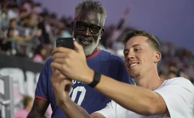 Miami Heat forward Duncan Robinson, right, takes a selfie for a fan in the stands, as he stands on the sideline before the start of an MLS soccer match between Inter Miami and Charlotte FC, Saturday, Sept. 28, 2024, in Fort Lauderdale, Fla. (AP Photo/Rebecca Blackwell)