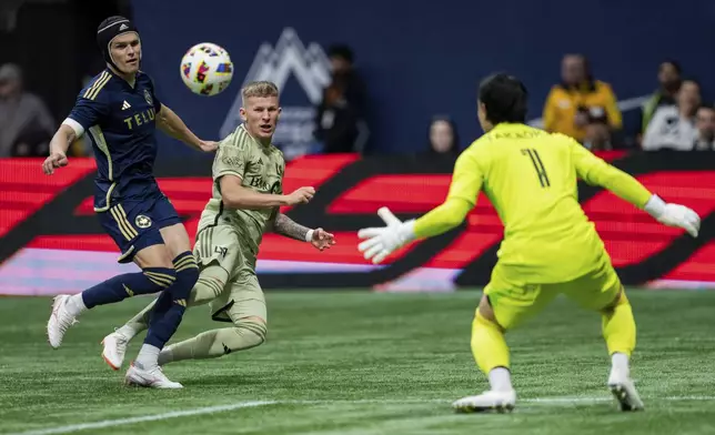 Los Angeles FC's Mateusz Bogusz, center, scores against Vancouver Whitecaps goalkeeper Yohei Takaoka, right, as Whitecaps' Bjorn Inge Utvik, left, defends during the first half of an MLS soccer match in Vancouver, British Columbia, Sunday, Oct. 13, 2024. (Ethan Cairns/The Canadian Press via AP)