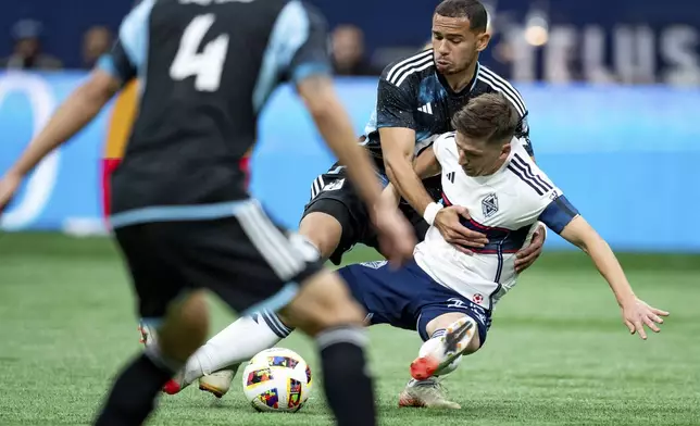 Minnesota United's Hassani Dotson, back left, knocks Vancouver Whitecaps' Ryan Gauld, right, over as they vie for the ball during the second half of an MLS soccer game, Saturday, Oct. 5, 2024 in Vancouver, British Columbia. (Ethan Cairns/Canadian Press via AP)