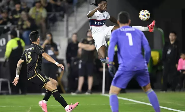 Vancouver Whitecaps defender Sam Adekugbe, center, kicks the ball against Los Angeles FC forward Cristian Olivera (13) and goalkeeper Hugo Lloris (1) during the first half of the first soccer match of an MLS Cup playoffs opening round in Los Angeles, Sunday, Oct. 27, 2024. (AP Photo/Alex Gallardo)