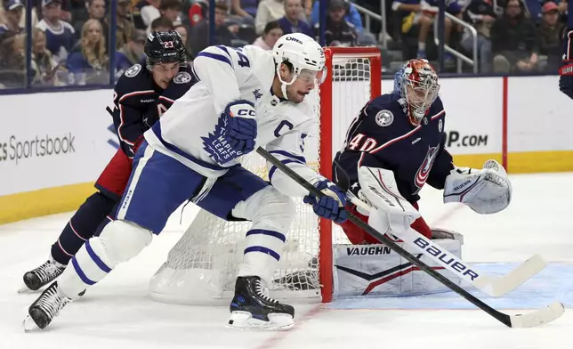 Toronto Maple Leafs forward Auston Matthews, center, controls the puck between Columbus Blue Jackets defenseman Sean Monahan, left, and goalie Daniil Tarasov during the first period of an NHL hockey game in Columbus, Ohio, Tuesday, Oct. 22, 2024. (AP Photo/Paul Vernon)