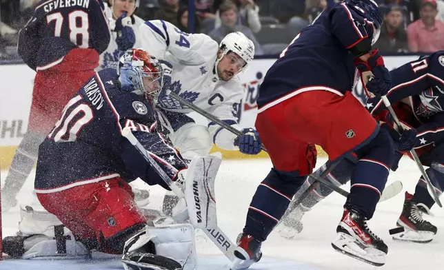 Columbus Blue Jackets goalie Daniil Tarasov, left, makes a stop behind Toronto Maple Leafs forward Auston Matthews, center, and Blue Jackets defenseman Ivan Provorov during the first period of an NHL hockey game in Columbus, Ohio, Tuesday, Oct. 22, 2024. (AP Photo/Paul Vernon)