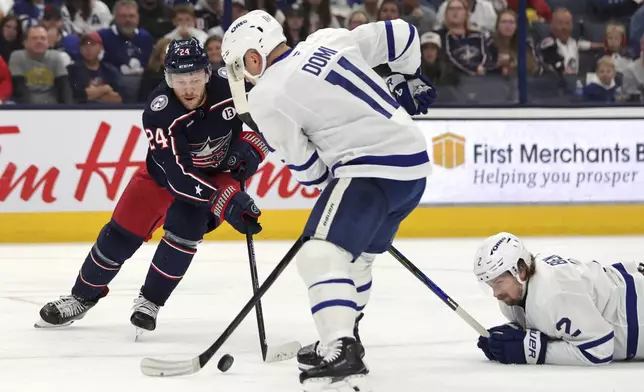 Columbus Blue Jackets forward Mathieu Olivier, left, reaches for the puck in front of Toronto Maple Leafs forward Max Domi, center, and forward Simon Benoit during the second period of an NHL hockey game in Columbus, Ohio, Tuesday, Oct. 22, 2024. (AP Photo/Paul Vernon)