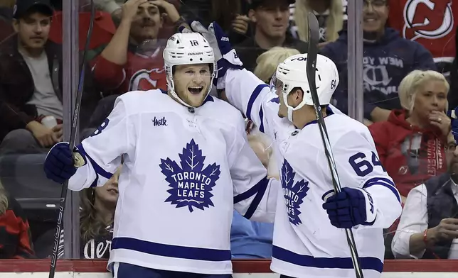 Toronto Maple Leafs center Steven Lorentz (18) is congratulated by David Kampf (64) after scoring during the first period of an NHL hockey game against the New Jersey Devils, Thursday, Oct. 10, 2024, in Newark, N.J. (AP Photo/Adam Hunger)